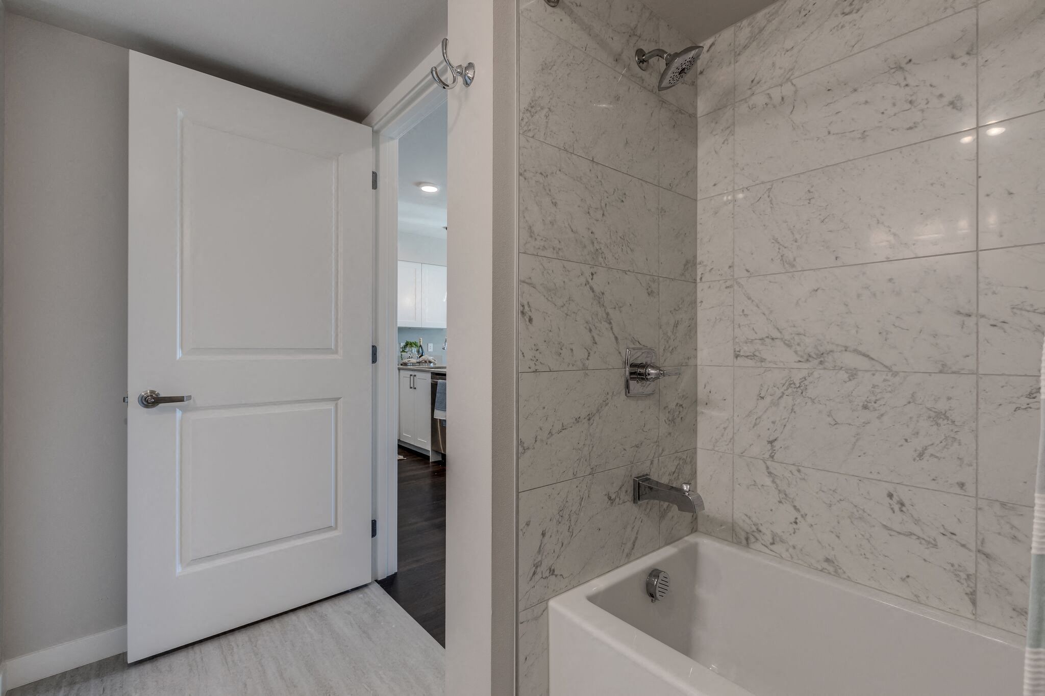 Lux Apartments Bellevue bathroom with floor to ceiling tiling in the bathtub and shower, and light-grey wood-style vinyl flooring